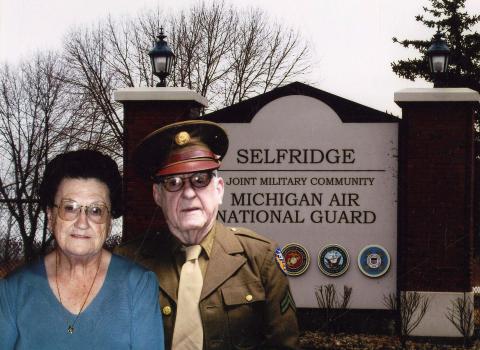 An image of Addie Blodgett (Left) and Earl Blodgett (Right) standing in front of a sign titled, "Selfridge Joint Military Community Michigan Air National Guard" 